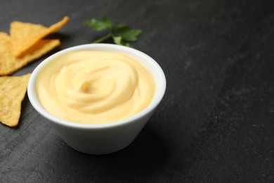 Photo of Tasty dipping cheese sauce in bowl, nacho chips and parsley on black table, closeup. Space for text