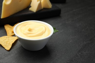 Photo of Tasty dipping cheese sauce in bowl and nacho chips on black table, closeup. Space for text