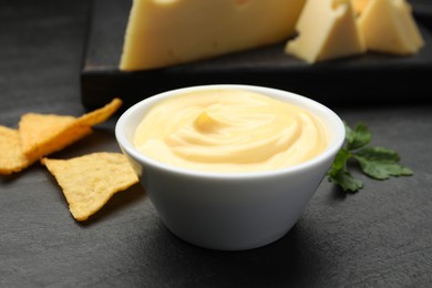 Photo of Tasty dipping cheese sauce in bowl, nacho chips and parsley on black table, closeup
