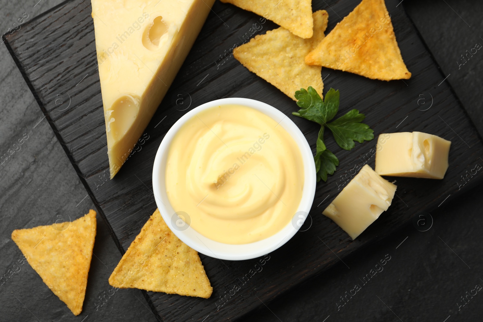 Tasty dipping cheese sauce in bowl, nacho chips and parsley on black table, top view Photo of Tasty dipping cheese sauce in bowl, nacho chips and parsley on black table, top view
