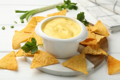 Photo of Tasty dipping cheese sauce in bowl and nacho chips on white wooden table, closeup
