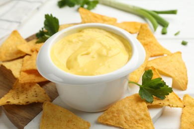 Photo of Tasty dipping cheese sauce in bowl and nacho chips on table, closeup