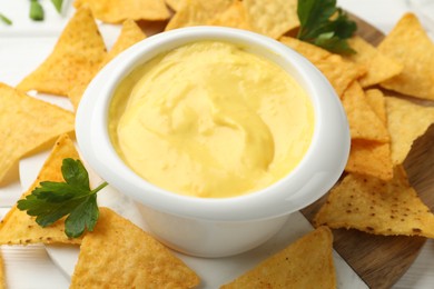 Photo of Tasty dipping cheese sauce in bowl and nacho chips on table, closeup