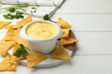Photo of Tasty dipping cheese sauce in bowl and nacho chips on white wooden table, closeup. Space for text