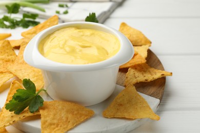 Photo of Tasty dipping cheese sauce in bowl and nacho chips on white wooden table, closeup