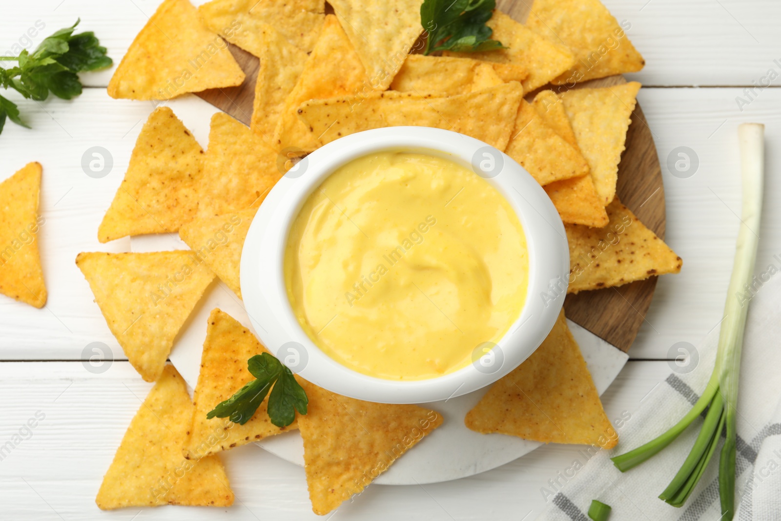Tasty dipping cheese sauce in bowl and nacho chips on white wooden table, flat lay Photo of Tasty dipping cheese sauce in bowl and nacho chips on white wooden table, flat lay