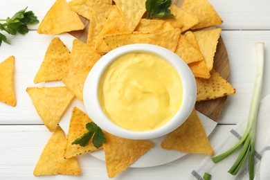 Photo of Tasty dipping cheese sauce in bowl and nacho chips on white wooden table, flat lay