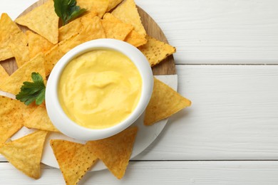 Photo of Tasty dipping cheese sauce in bowl and nacho chips on white wooden table, top view. Space for text