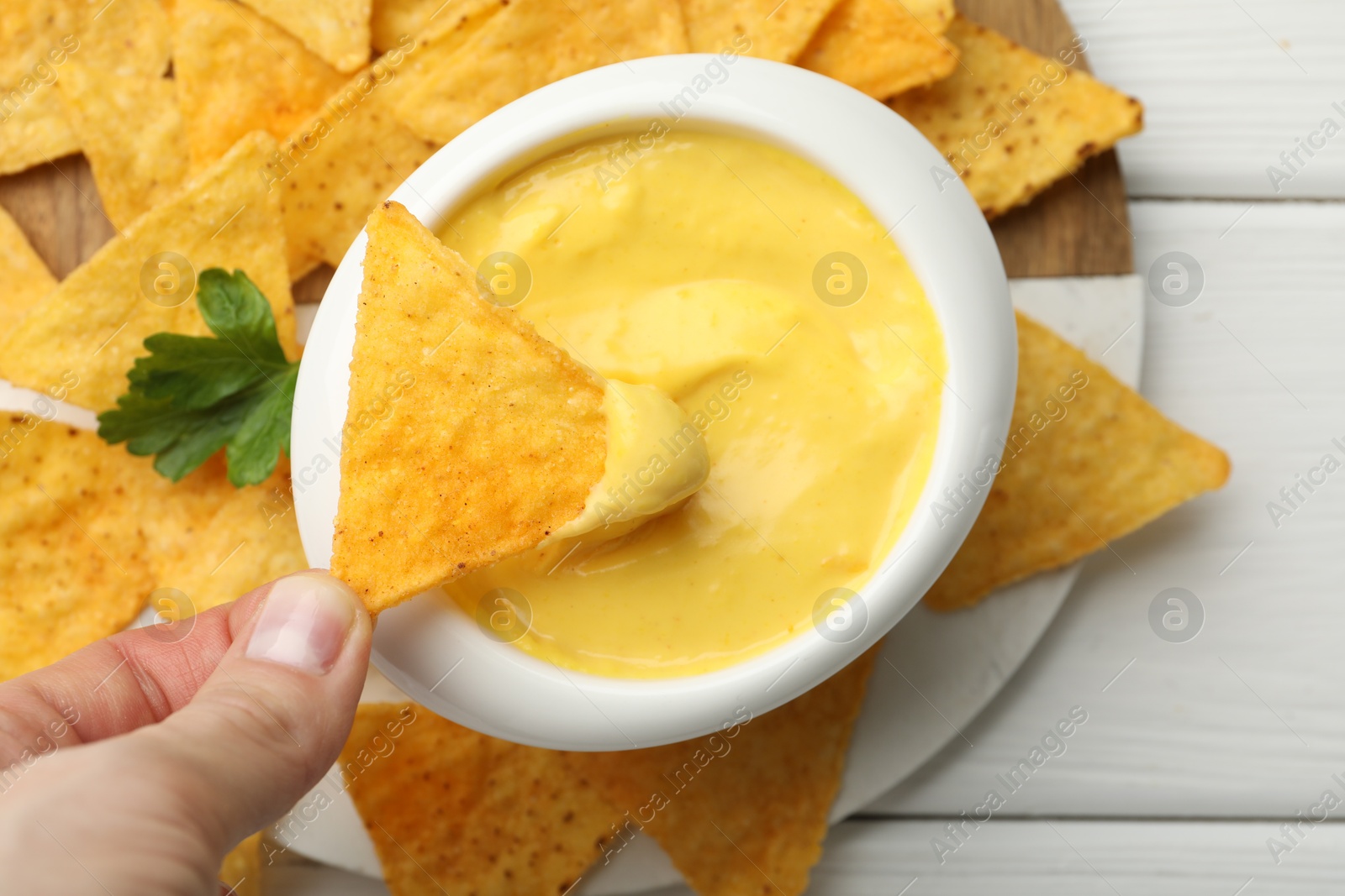 Woman dipping nacho chip into tasty cheese sauce at white wooden table, top view Photo of Woman dipping nacho chip into tasty cheese sauce at white wooden table, top view