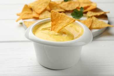Photo of Tasty dipping cheese sauce in bowl and nacho chips on white wooden table, closeup