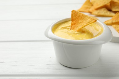 Photo of Tasty dipping cheese sauce in bowl and nacho chips on white wooden table, closeup. Space for text
