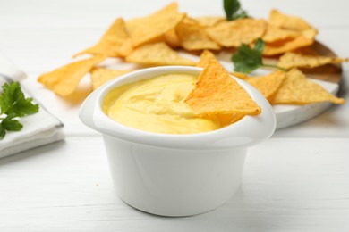 Photo of Tasty dipping cheese sauce in bowl and nacho chips on white wooden table, closeup
