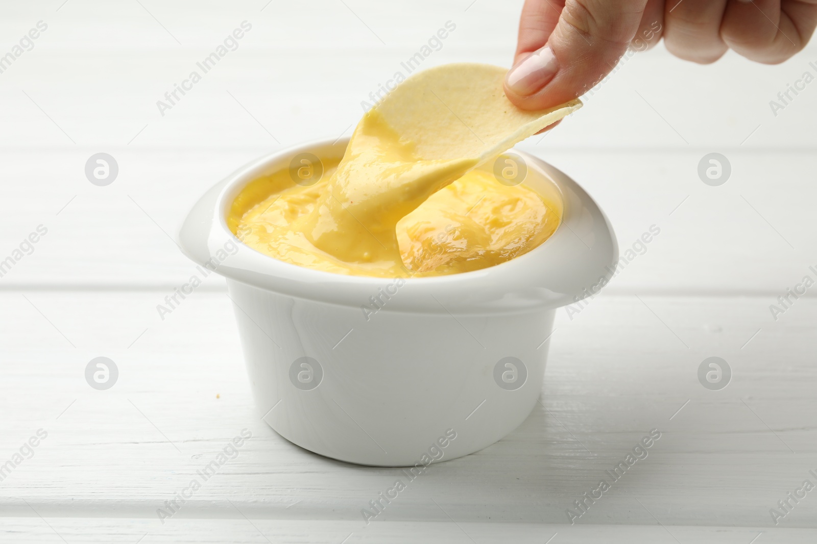 Woman dipping potato chip into tasty cheese sauce at white wooden table, closeup Photo of Woman dipping potato chip into tasty cheese sauce at white wooden table, closeup