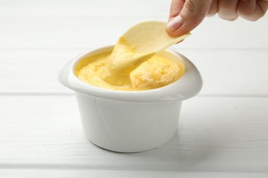 Photo of Woman dipping potato chip into tasty cheese sauce at white wooden table, closeup