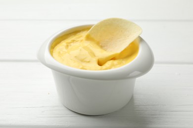 Photo of Tasty dipping cheese sauce in bowl and potato chip on white wooden table, closeup