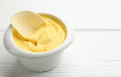 Photo of Tasty dipping cheese sauce in bowl and potato chip on white wooden table, closeup. Space for text