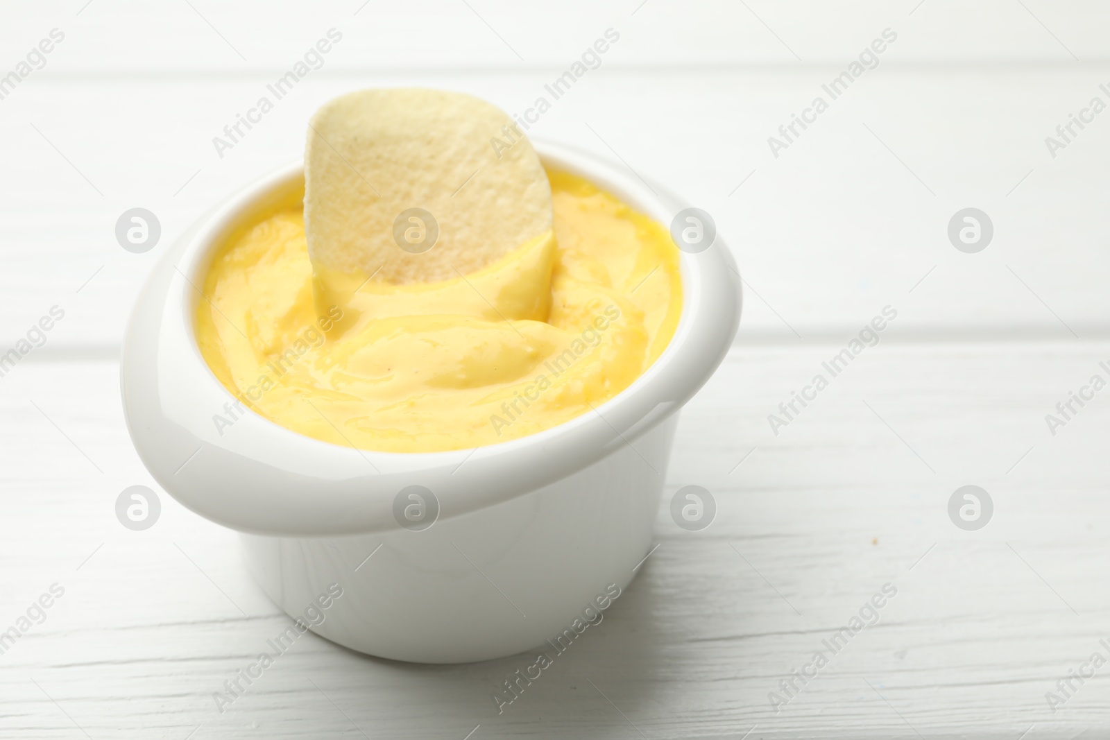 Tasty dipping cheese sauce in bowl and potato chip on white wooden table, closeup. Space for text Photo of Tasty dipping cheese sauce in bowl and potato chip on white wooden table, closeup. Space for text