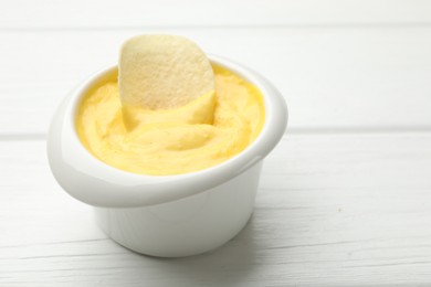 Photo of Tasty dipping cheese sauce in bowl and potato chip on white wooden table, closeup. Space for text