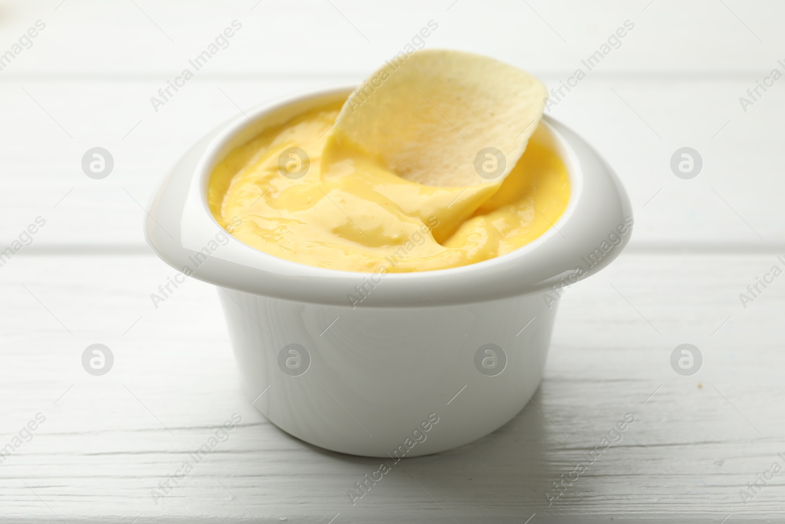 Tasty dipping cheese sauce in bowl and potato chip on white wooden table, closeup Photo of Tasty dipping cheese sauce in bowl and potato chip on white wooden table, closeup