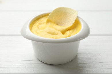 Photo of Tasty dipping cheese sauce in bowl and potato chip on white wooden table, closeup
