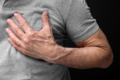 Photo of Heart attack. Senior man suffering from pain in chest on black background, closeup