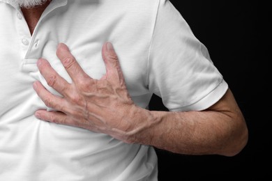 Photo of Heart attack. Senior man suffering from pain in chest on black background, closeup