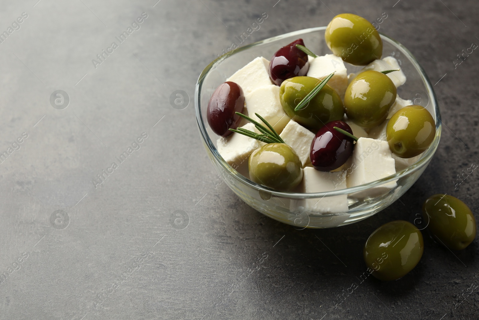 Tasty olives with feta cheese in glass bowl on grey textured table, closeup. Space for text Photo of Tasty olives with feta cheese in glass bowl on grey textured table, closeup. Space for text