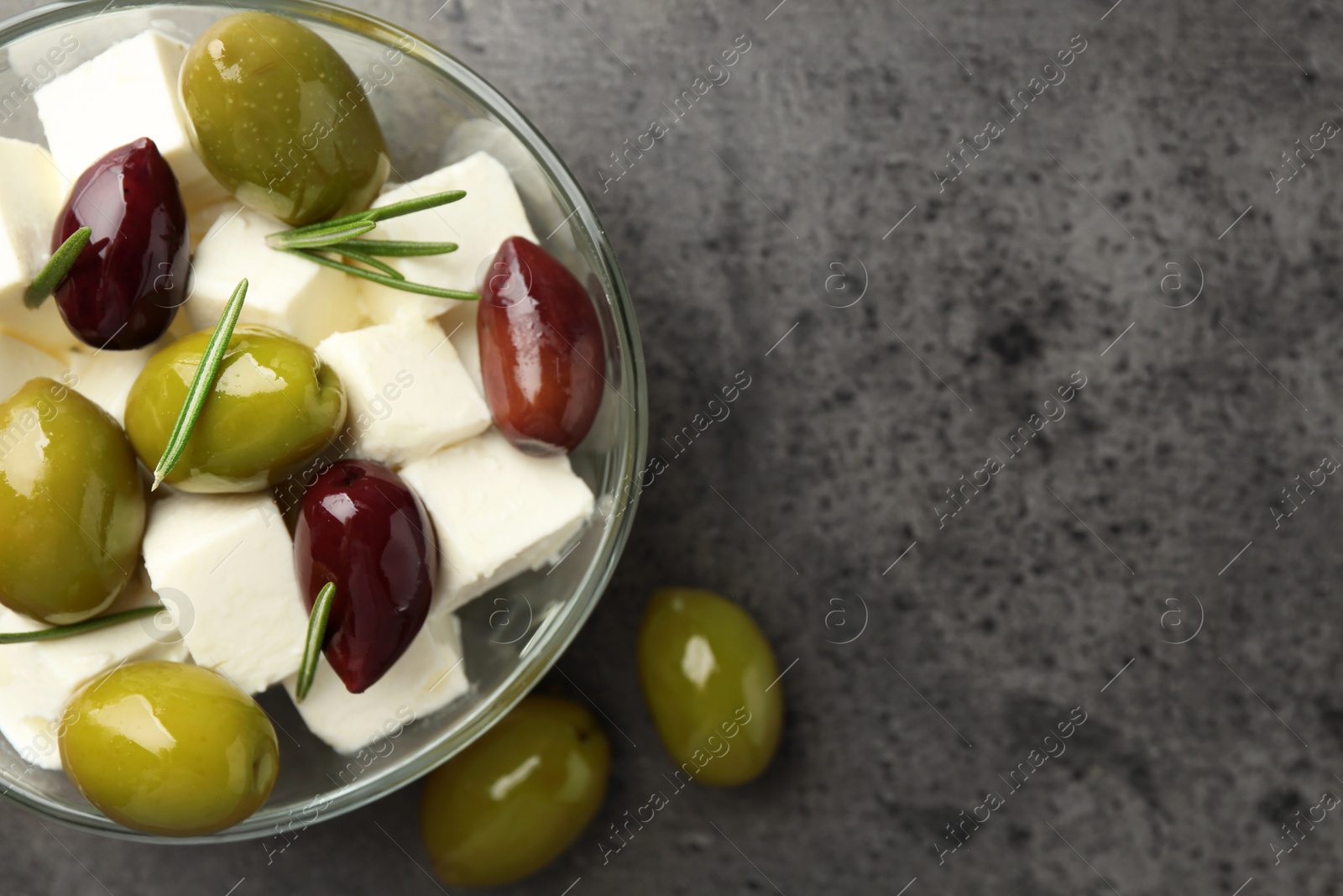 Tasty olives with feta cheese in glass bowl on grey textured table, top view. Space for text Photo of Tasty olives with feta cheese in glass bowl on grey textured table, top view. Space for text