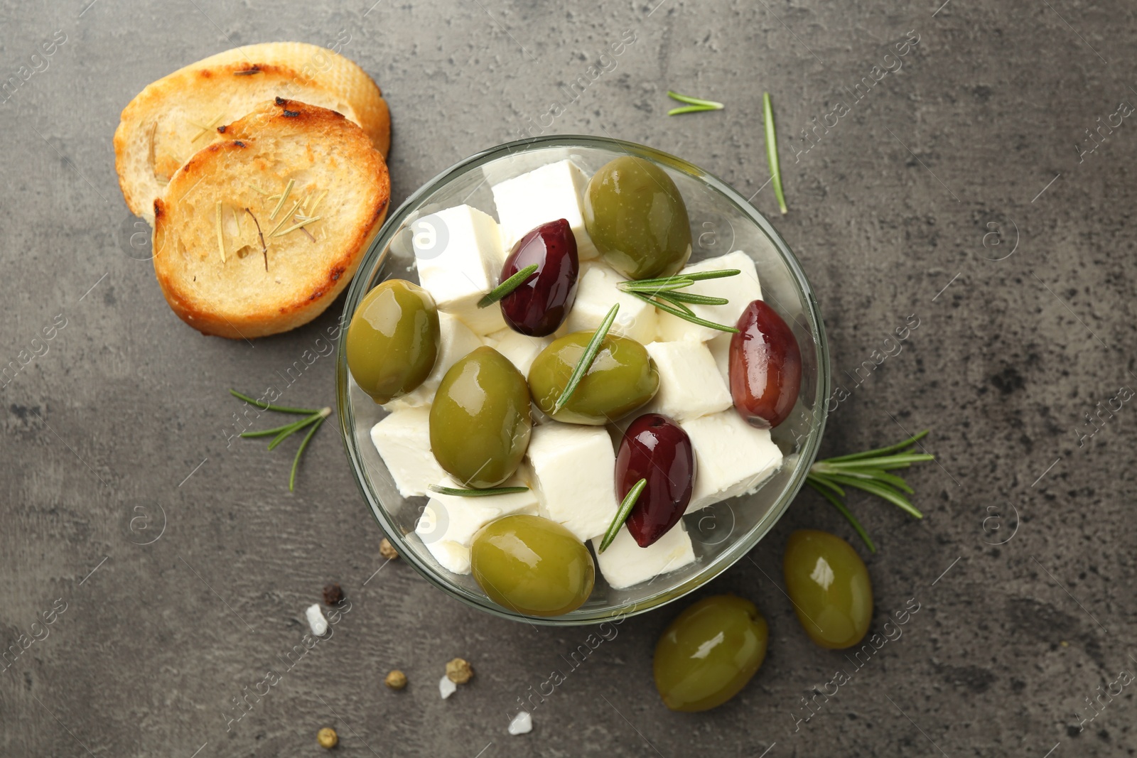 Tasty olives served with feta cheese and bread on grey textured table, flat lay Photo of Tasty olives served with feta cheese and bread on grey textured table, flat lay