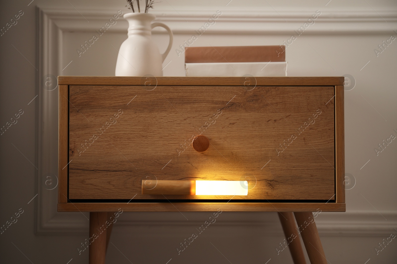 Photo of Glowing modern LED lamp on wooden bedside table indoors