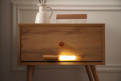 Photo of Glowing modern LED lamp on wooden bedside table indoors