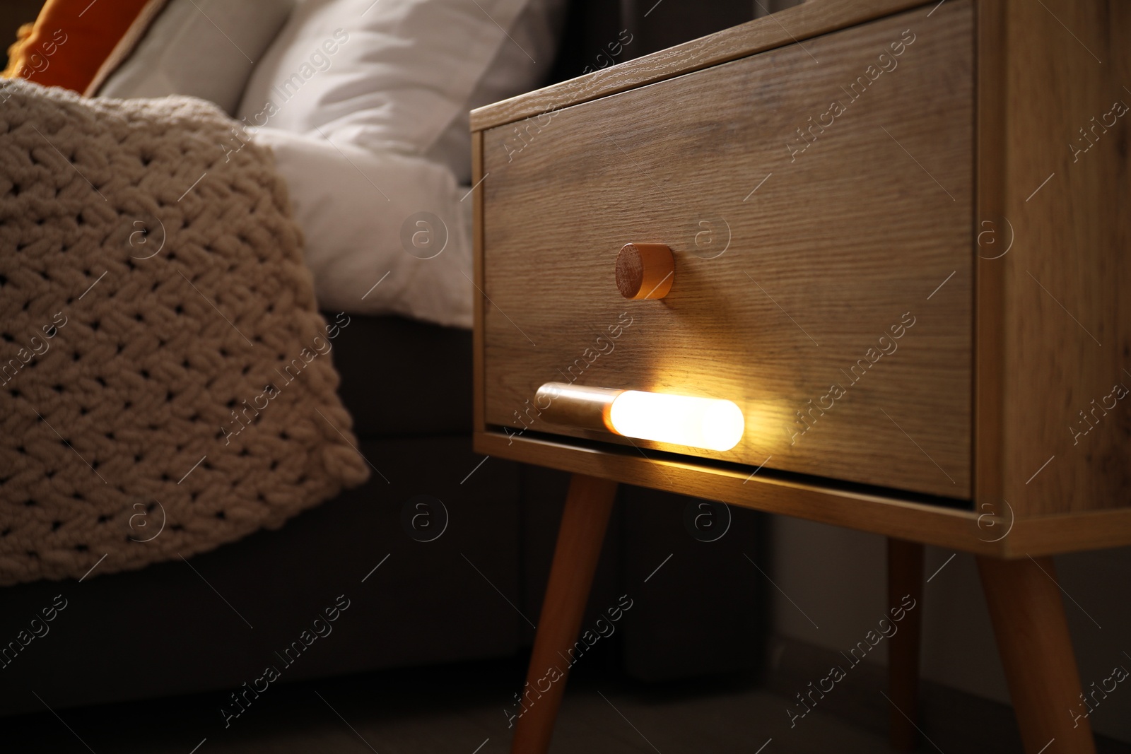 Photo of Glowing modern LED lamp on wooden bedside table indoors, closeup