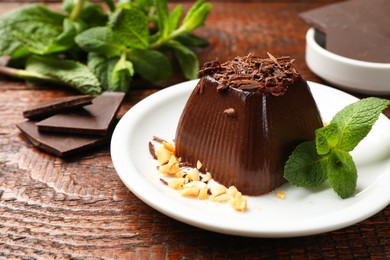 Photo of Tasty pudding with peanuts, mint and pieces of chocolate on wooden table, closeup