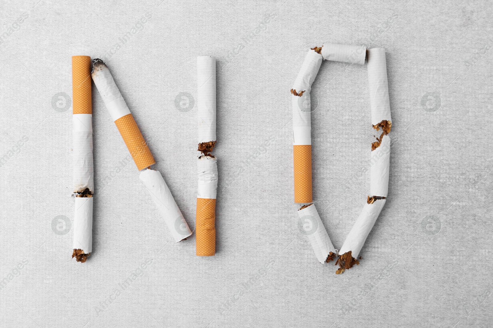 Photo of Word NO made with cigarette butts on light gray background, top view