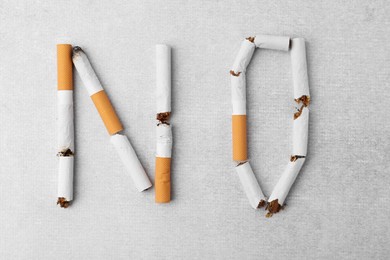 Photo of Word NO made with cigarette butts on light gray background, top view