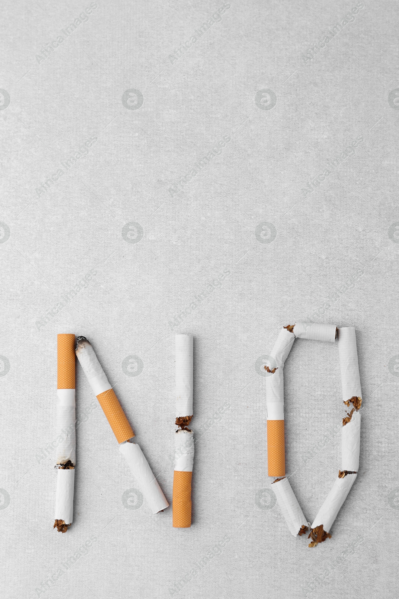 Photo of Word NO made with cigarette butts on light gray background, top view. Space for text