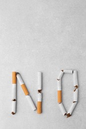 Word NO made with cigarette butts on light gray background, top view. Space for text