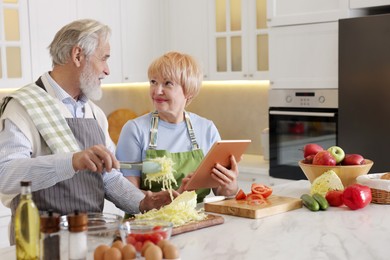 Photo of Senior couple using tablet while cooking together in kitchen