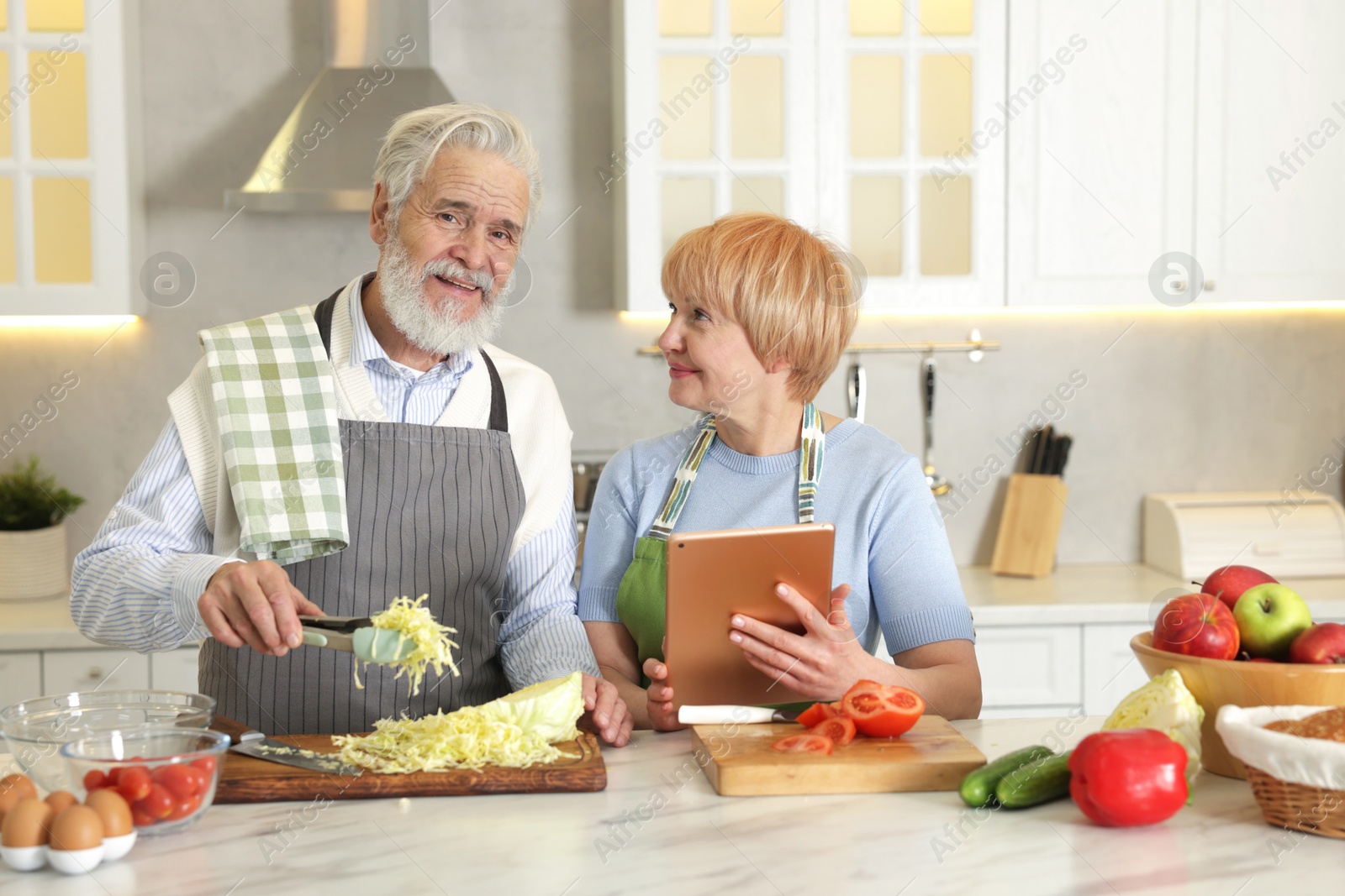 Photo of Senior couple using tablet while cooking together in kitchen