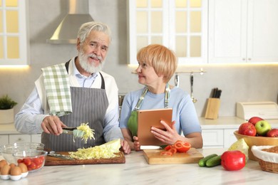 Senior couple using tablet while cooking together in kitchen