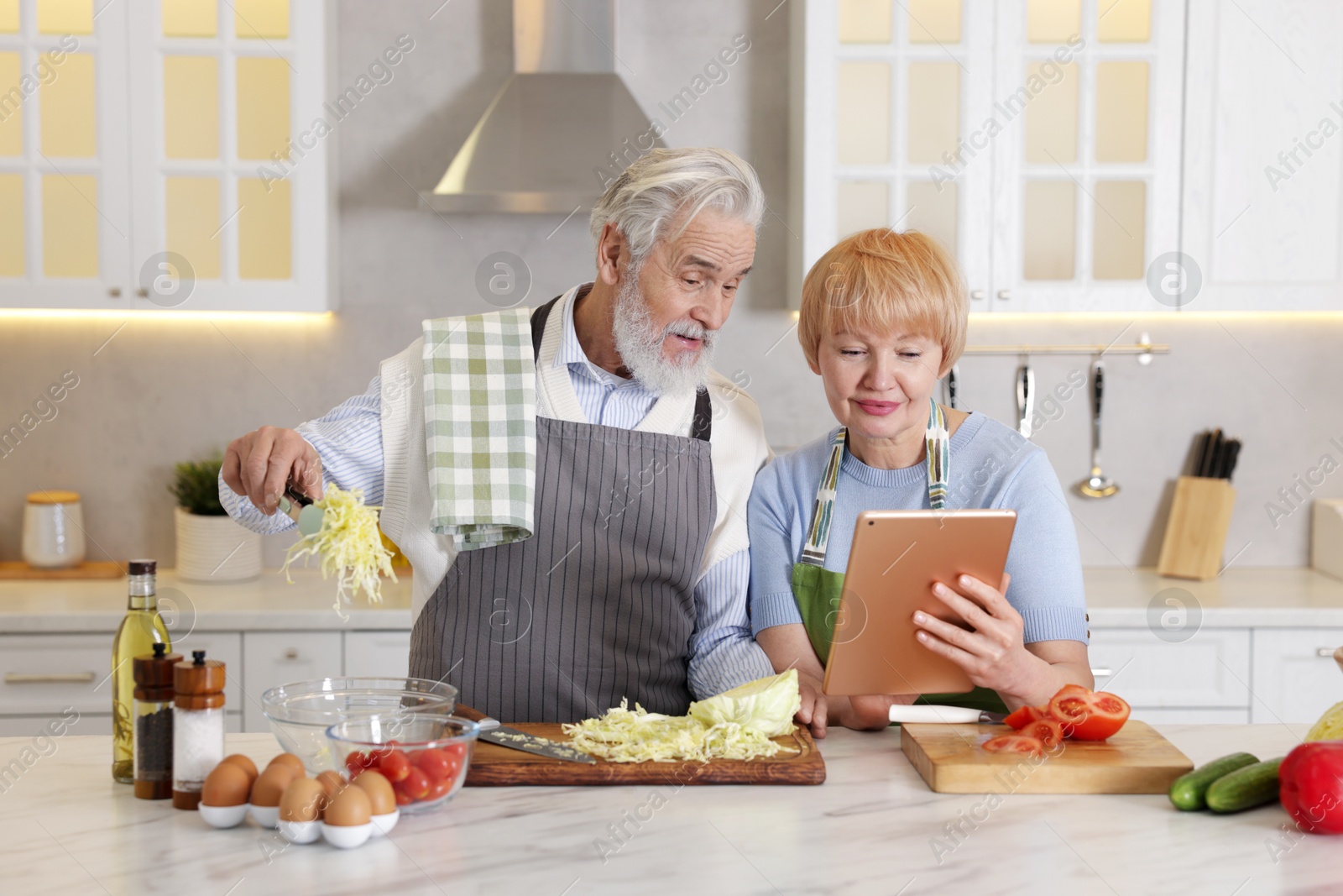 Photo of Senior couple using tablet while cooking together in kitchen