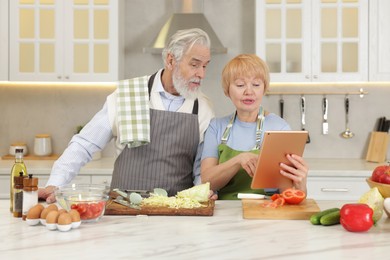 Photo of Senior couple using tablet while cooking together in kitchen