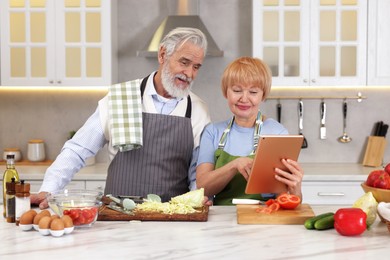 Photo of Senior couple using tablet while cooking together in kitchen