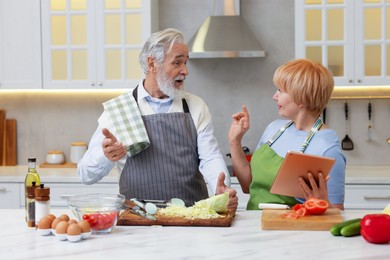 Photo of Senior couple using tablet while cooking together in kitchen