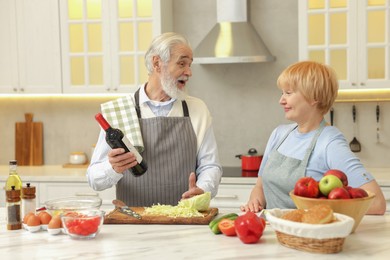 Photo of Senior man suggesting wine to his wife while cooking in kitchen