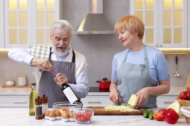 Photo of Senior man opening bottle of wine while cooking with his wife in kitchen