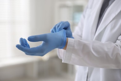 Photo of Doctor putting on medical gloves in hospital, closeup