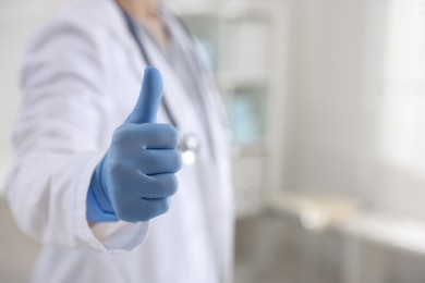 Photo of Doctor in medical gloves showing thumbs up indoors, closeup. Space for text