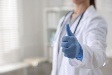 Doctor in medical gloves showing thumbs up indoors, closeup. Space for text