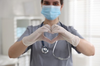 Medical worker in gloves making heart with hands indoors, selective focus